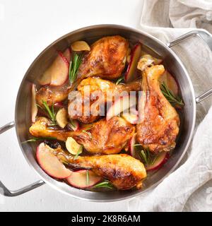 Bastoncini di pollo cotti con mele ed erbe in pentola su fondo bianco. Vista dall'alto, disposizione piatta Foto Stock