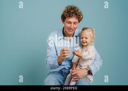 Il giovane riccio e la figlia sorridono mentre si posano con lecca isolata su sfondo blu Foto Stock