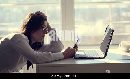 Una giovane lavoratrice d'ufficio naviga sui social network su un telefono cellulare, durante la giornata di lavoro, in ufficio. Una breve pausa, riposarsi sul lavoro. Possibile concetto di dipendente senza scrupoli e pigro o stanco. Foto di alta qualità Foto Stock