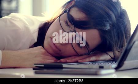 Donna d'affari sovraccarica, esausta e stanca con occhiali, riposante, addormentata su un laptop in una scrivania in ufficio. È sopraffatta dal lavoro, dalle riprese di ritratti. Foto di alta qualità Foto Stock