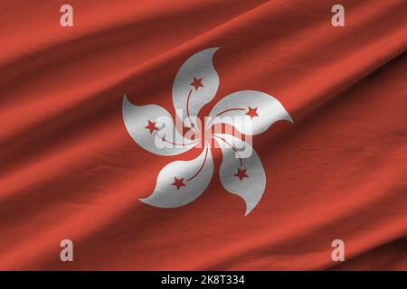 Bandiera di Hong kong con grandi pieghe che sventolano da vicino sotto la luce dello studio in interni. I simboli e i colori ufficiali in tessuto banner Foto Stock