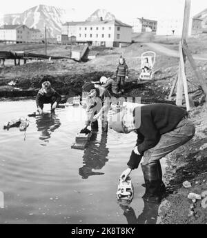 Svalbard, Longyearbyen 1963. Alcuni lavoratori del negozio Norske hanno avuto l'opportunità di portare la famiglia a Svalbard. I bambini dei minatori giocano all'aperto. Anche in estate, devono indossare abiti invernali. Qui i ragazzi hanno reso le strutture portuali con le barche in un piccolo stagno, una ragazza si adatta i piccoli fratelli sullo sfondo era comune per un minatore a lavorare per 10 anni prima di poter ottenere una casa per la sua famiglia a Svalbard. Foto: Aage Storløkken / corrente / NTB Foto Stock