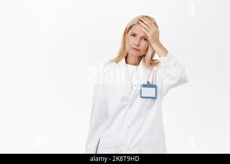 Ritratto di una donna anziana stanca medico, mal di testa, toccare la fronte e guardare male, sentirsi male, in piedi su sfondo bianco Foto Stock