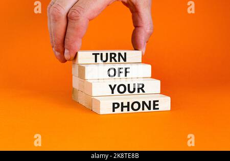 Disattivare il simbolo del telefono. Le parole concettuali spengono il telefono su blocchi di legno. Bellissimo sfondo arancione. Mano uomo d'affari. Psicologico aziendale Foto Stock