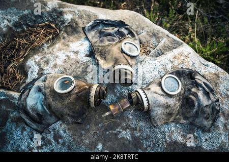 tre vecchie maschere a gas usate si trovano su un grande masso nella foresta Foto Stock