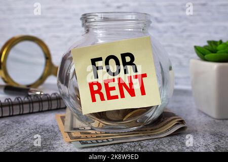 Affitto. Vaso di vetro con monete e un iscrizione affitto. Chi detiene moneta in mano Foto Stock