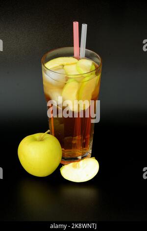 Succo di frutta in un bicchiere alto con ghiaccio e pezzi su fondo nero, accanto a mele verdi mature. Posizionamento verticale. Foto Stock