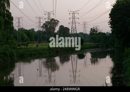 Cavi elettrici sospesi portati su Pylons attraversando un fiume tranquillo e tranquillo. I cavi sono sospesi e riflessi nel fiume. Molto tranquillo. Foto Stock
