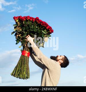 Uomo con bouquet di fiori di rose. L'uomo bearded tiene un grande bouquet di rose rosse, proponga al boyfriend sulla data. Romantico ragazzo celebrare San Valentino Foto Stock