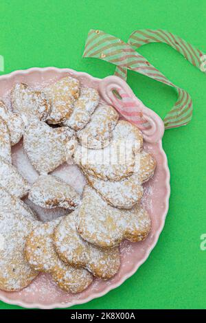 Biscotti tradizionali fatti in casa (zampe) serviti su un piatto scuro con noci di rosa e macadamia sul tavolo verde. Design concettuale. Foto Stock