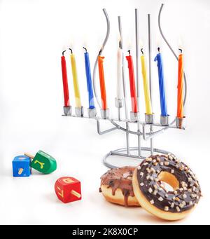 Vacanza ebraica sfondo Hanukkah. Il piatto tradizionale è costituito da ciambelle dolci. Hanukkah tavolo impostazione candelabro con candele e spinning cime su bianco Foto Stock