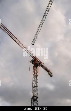 Sagome di gru edili e edificio residenziale incompiuto contro l'alba sopra la città. Edilizia abitativa, condominio costruzione di nuovi edifici residenziali. Sullo sfondo del cielo del tramonto. Foto Stock