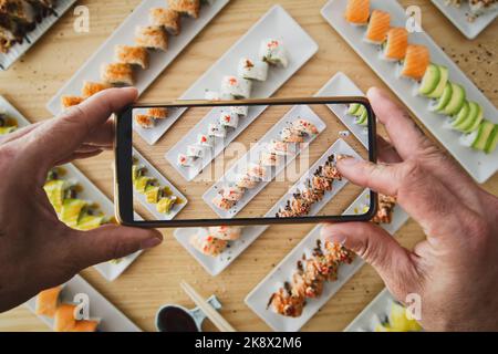 Uomo che scatta foto di cibo giapponese. Sushi, california roll Foto Stock