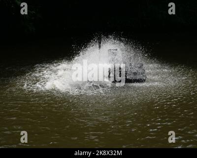 Gruppo di goccioline d'acqua spruzzate dal colpo della turbina con fondo nero, ruota a pale che colpisce la superficie di acqua verde per aggiungere ossigeno Foto Stock