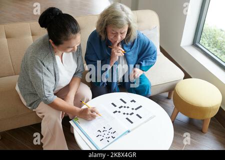 Seri amici anziani che discutono la risposta per il puzzle di cruciverba, vista dall'alto Foto Stock