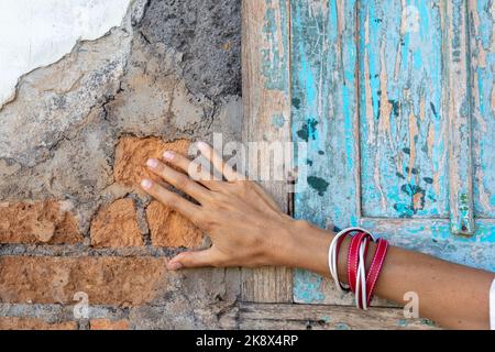 La mano della ragazza con i braccialetti di cuoio rosso e bianco sullo sfondo del vecchio muro di mattoni. Accessori urbani. Foto Stock