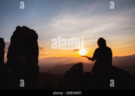 silhouette di uomo alzarsi mano in preghiera in cima alla montagna e tramonto cielo sfondo astratto. Concetto di libertà e avventura di viaggio. Foto Stock