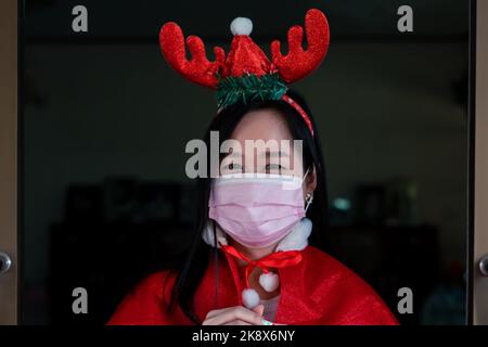 Bella donna asiatica che indossa un costume di Babbo Natale e una maschera per il viso tiene nel festival "il giorno di Natale" a casa Foto Stock