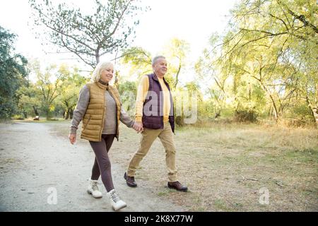 Coppia matura che tiene hans mentre cammina nella foresta in una giornata fredda e soleggiata Foto Stock