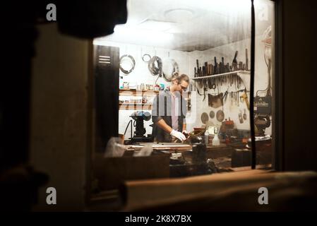 Questo è dove faccio la mia magia. Un giovane falegname maschio concentrato che lavora duro nel suo laboratorio a casa durante la notte. Foto Stock
