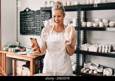 Un'altra ciotola completato oggi. Una donna matura attraente usando il suo cellulare per prendere un selfie con la sua ceramica nel suo studio. Foto Stock