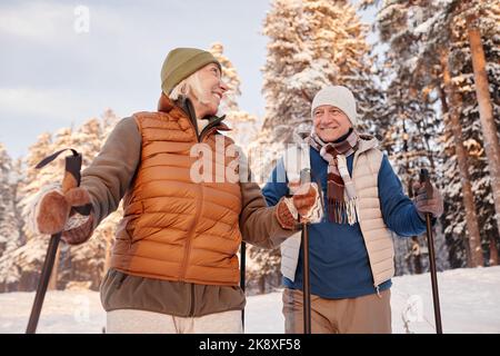 Basso angolo ritratto di felice coppia senior a piedi con pali nella foresta invernale e sorridente Foto Stock