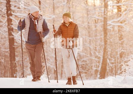 Ritratto completo di coppia anziana attiva godendo Nordic Walk con i pali nella bella foresta invernale Foto Stock