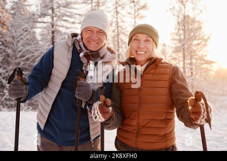 Vita in su ritratto di coppia anziana attiva godendo Nordic Walk con i pali nella foresta invernale e guardando la macchina fotografica Foto Stock