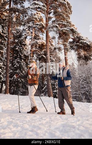 Lunghezza intera di coppia sportiva senior godendo Nordic Walk con escursioni in racchette nella foresta d'inverno Foto Stock