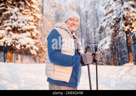 Vita in su ritratto di un uomo sorridente maturo godendo Nordic Walk nella foresta d'inverno al tramonto, copia spazio Foto Stock