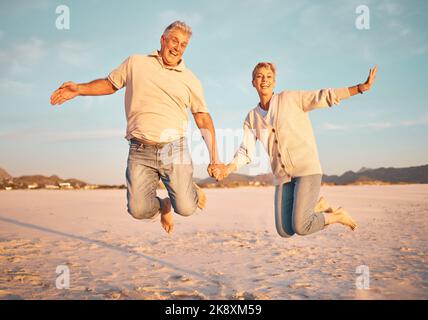 La coppia, la spiaggia e gli anziani attivi tengono le mani mentre saltano nella sabbia, felici ed eccitati al tramonto. Amore, famiglia e libertà con uomo e donna maturi Foto Stock