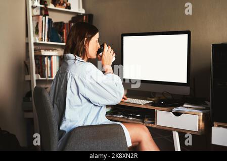 Questa è la vita di un imprenditore: Una giovane e attraente donna d'affari seduta da sola nel suo ufficio domestico e bevendo una tazza di caffè. Foto Stock