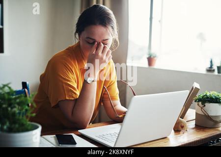 È troppo stressante. Una giovane e attraente donna d'affari seduta da sola nel suo ufficio domestico e sentendosi stressata mentre usa il suo laptop. Foto Stock