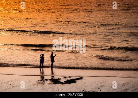 Due vacanzieri si sono stagliati sulla costa di Fistral Beach al tramonto a Newquay in Cornovaglia nel Regno Unito in Europa. Foto Stock