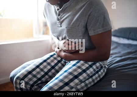 Un uomo irriconoscibile seduto da solo sul letto e sofferente di crampi allo stomaco mentre si è a casa da solo. Foto Stock