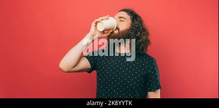 Banner dimensione foto di uomo orrido con lunga tazza di caffè bere capelli per andare su sfondo rosa. Foto Stock