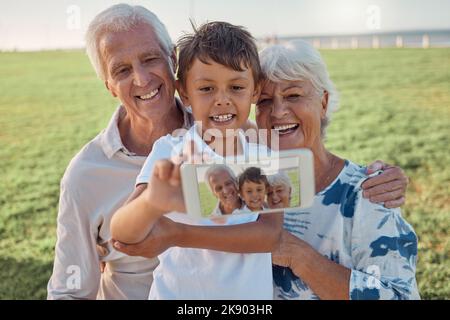 Telefono, selfie e nonni felici con bambino all'aperto in natura in famiglia pic-nic insieme. Felicità, sorriso e anziano uomo e donna in pensione Foto Stock