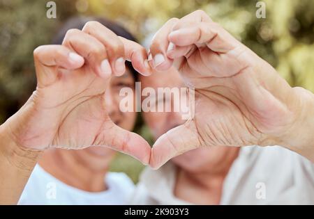 Mani di cuore, amore e coppia anziana, felicità e gentilezza, fiducia e sostegno nel parco giardino. Primo piano matrimonio, forma dito e celebrare la cura Foto Stock