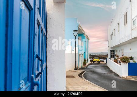 Auto gialla a 4 ruote motrici sulla strada stretta con edifici bianchi e blu a Corralejo, Lanzarote, Isole Canarie, Spagna Foto Stock