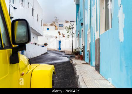 Auto gialla a 4 ruote motrici sulla strada stretta con edifici bianchi e blu a Corralejo, Lanzarote, Isole Canarie, Spagna Foto Stock