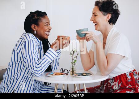 Due donne d'affari felici ridendo e avendo caffè insieme in un caffè ufficio. Due donne d'affari allegre che si godono un caffè amichevole riunione in un mod Foto Stock
