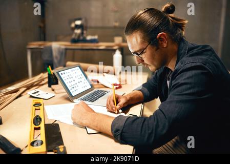 Ha competenze di livello successivo, un giovane falegname maschio concentrato che lavora su un progetto all'interno di un laboratorio di notte. Foto Stock