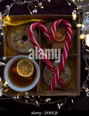 Accogliente e deliziosa foto d'atmosfera sul tema del Capodanno. Una tazza con fettine di tè e limone, biscotti, ghirlande luminose, lecca-lecca ripiegata a forma di Foto Stock