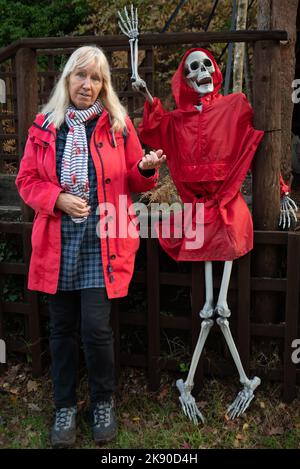 Donna in un cappotto rosso con scheletro in un cappotto rosso, Halloween alla riserva naturale della piscina blu, Wareham, Purbeck, Dorset, Regno Unito Foto Stock