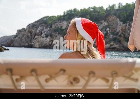 donna anziana con cappello di natale seduto guardando il mare in vacanza di natale Foto Stock