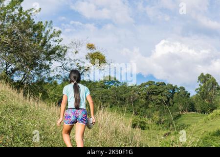 latina brunette ragazza che cammina in cima ad una montagna in un giorno d'estate. ragazza contadina a capelli lunghi che cammina attraverso un pascolo in cima ad un monte sudamericano Foto Stock