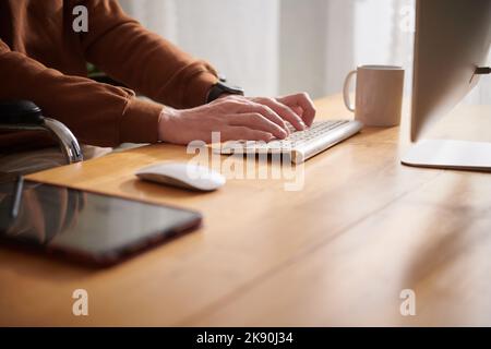 Immagine di primo piano di un uomo con disabilità seduto alla scrivania dell'ufficio di casa e al lavoro sul computer Foto Stock