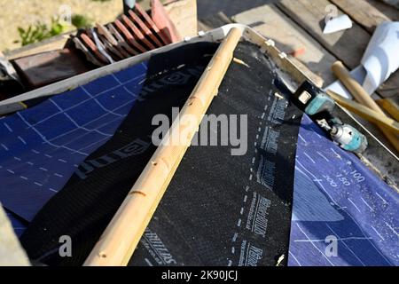 Lavori di copertura su argilla tegola residenziale Hipped Bay tetto, montaggio di membrana di sfiato sotto l'anca rafter che avrà piombo lampeggiante Foto Stock