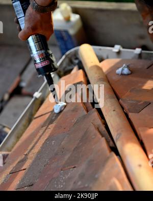 Lavori di copertura su tegole di argilla residenziale hipped Bay tetto, applicando adesivo per tenere le tegole tagliate per il montaggio angolo taglio alla caraffa Foto Stock