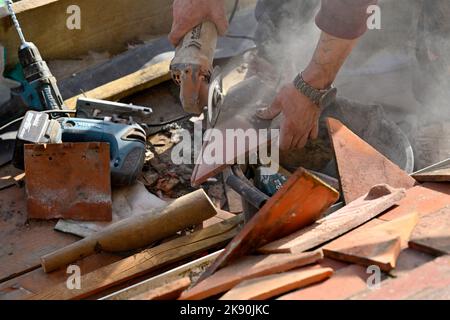 Lavori di copertura su tegole di argilla residenziale hipped Bay tetto, taglio tegole di argilla con smerigliatrice angolare Foto Stock